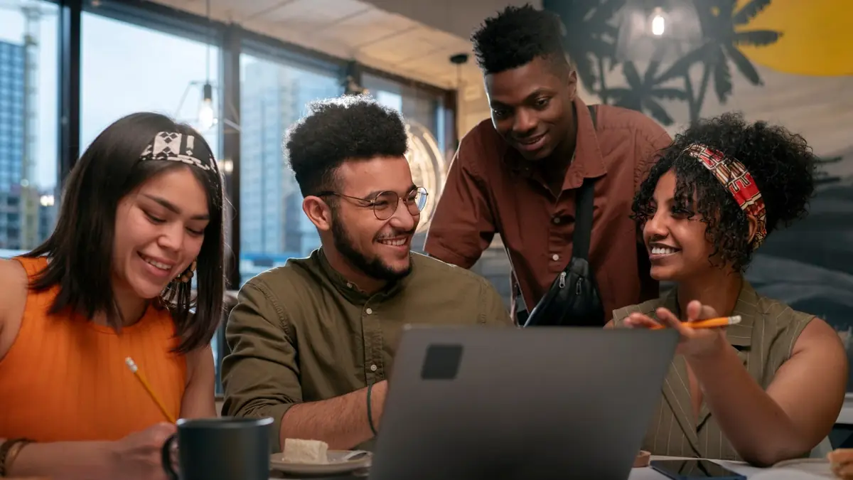 A team gathered around a laptop, smiling and working together—bringing project management to life through chat tools.