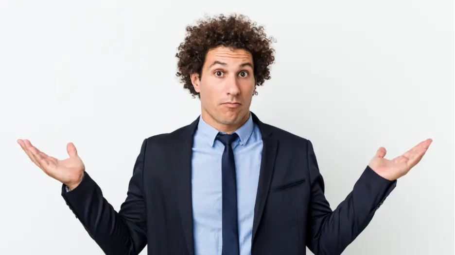 Confused businessman in a suit shrugging with raised hands, symbolizing uncertainty about communication choices. The image illustrates the challenges organizations face before adopting Microsoft Teams Operator Connect for streamlined calling and connectivity.