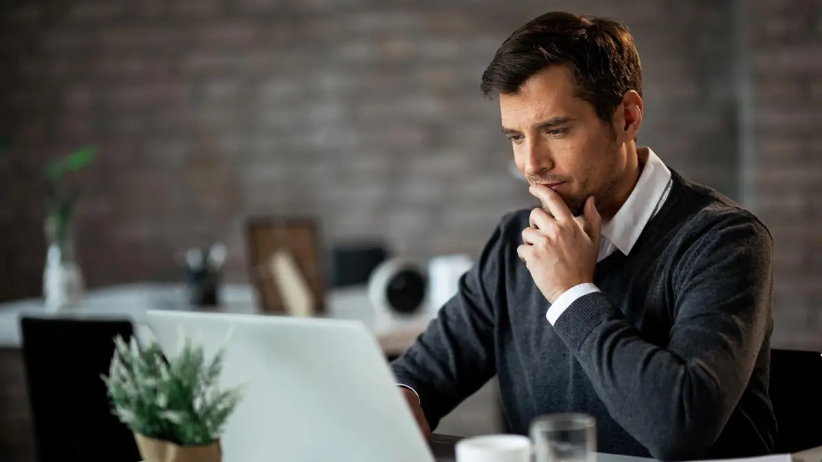 A man sitting thoughtfully in front of a laptop, pondering how to enable public switched telephone network (PSTN) connectivity to Microsoft Teams.