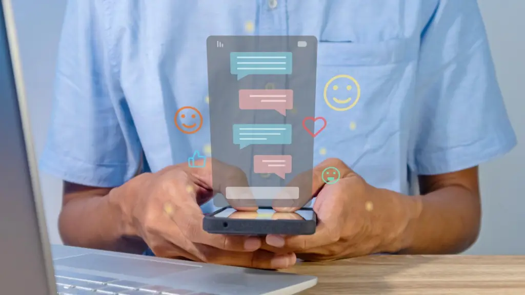 A person in a light blue shirt uses a smartphone with digital chat bubbles and social icons (like hearts and smiley faces) floating above the screen. The image represents real-time messaging across platforms, enabled by federated chat technology for seamless, unified communication.